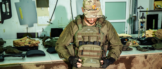 Fitting an ArmorIQ plate carrier in the workshop, with armor plates on the bench behind