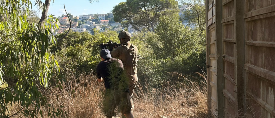 Two operators moving through woodland, one in a plate carrier and helmet