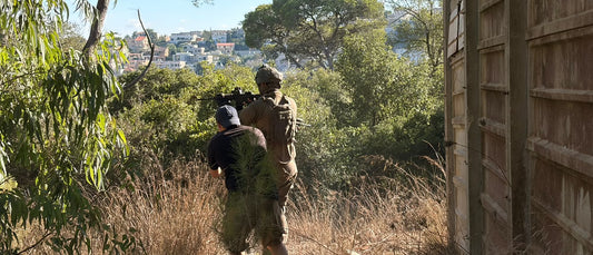 Two operators moving through woodland, one in a plate carrier and helmet